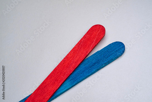 A minimalist studio shot of a red and blue wooden craft stick overlapping on a textured surface. Representing political contrast, bipartisan cooperation or creative education concepts.