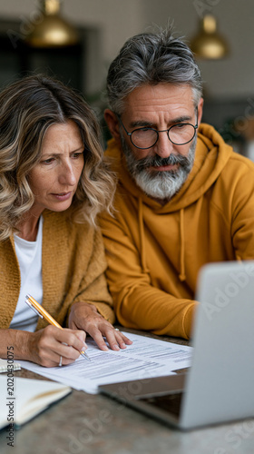 Financial Focus: A mature couple engages in a financial discussion, their attention fixed on a laptop screen while working with paperwork. A scene reflecting responsibility, diligence.