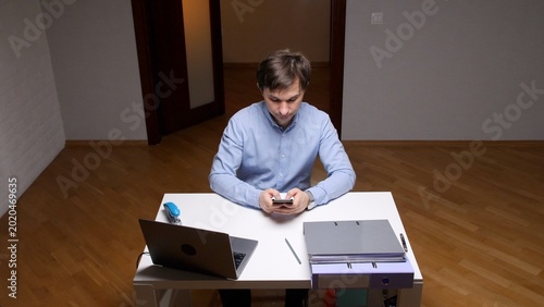 Foto Young man in a home office engrossed in his smartphone, scrolling social apps an