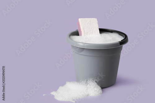 Plastic bucket of foam with sponge on purple background