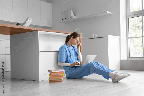 Tired female medical intern studying with laptop in clinic