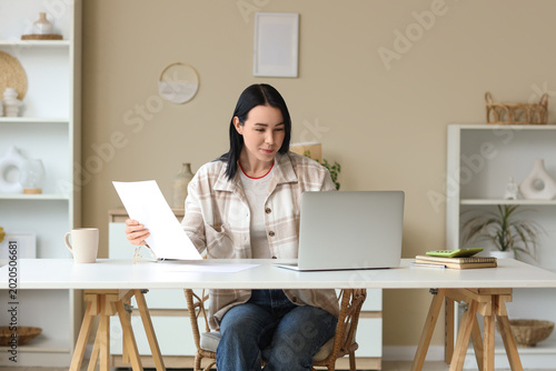 Young woman with refund form using laptop at table in room
