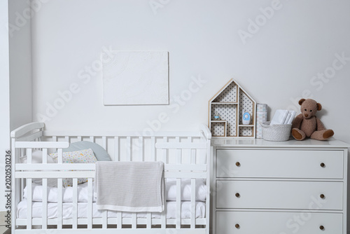 Photos Interior of children's room with crib and chest of drawers near white wall