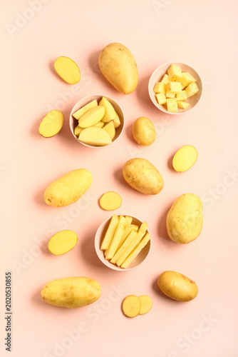 Bowls with cut and whole potatoes on pink background