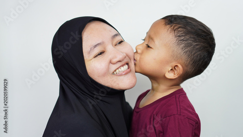 Foto A little Asian boy is kissing his mother, a Muslim woman wearing a hijab, with a