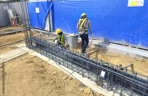 Tableau sur toile Two construction workers tying steel reinforcement for ground beam inside industrial factory