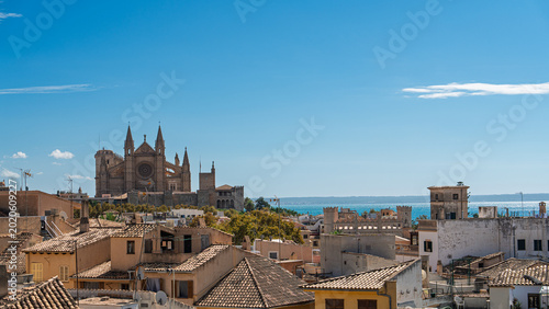 Bild auf Leinwand Aerial view of Palma Cathedral in Mallorca, Spain, with city rooftops and the Mediterranean Sea visible beyond under bright clear skies on a sunny day, showing historic stone
