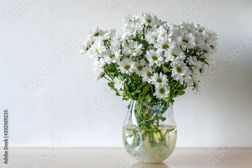 A bouquet of white Bacardi Chrysanthemum flowers in a glass vase on a wooden table.