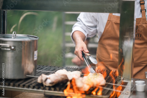 Barbecue grill with chef cooking chicken over open flame in outdoor kitchen