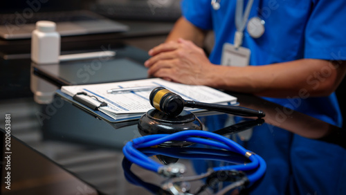 Konstfotografi Medical legal concept: judge gavel and stethoscope on desk with nurse or doctor in background, clipboard paperwork and blurred office setting