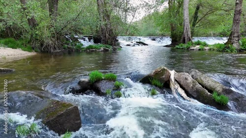 Aerial view of Rio Arnoia flowing over rocks and small waterfalls surrounded by lush green trees and vegetation in Ourense, Ourense, Spain.