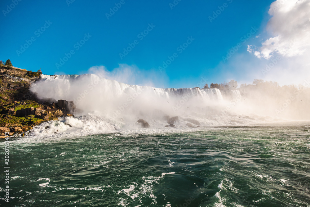 Naklejka premium Niagara Falls powerful waterfall landscape with mist and rushing water under blue sky