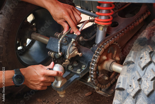 Focused mechanic performing careful repair on an offroad atv suspension system adjusting metal chain and rear axle with greasy hand next to rubber wheel outside