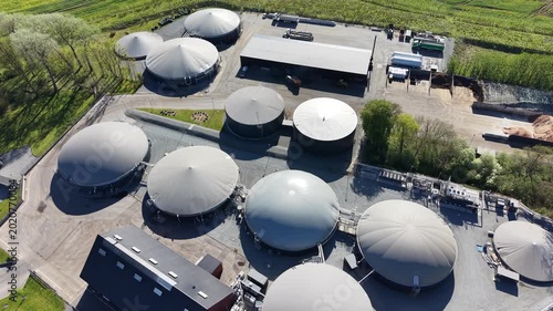 High-angle drone shot capturing the circular storage tanks and infrastructure of a biogas facility near Hammel, Denmark, during a sunny spring day.