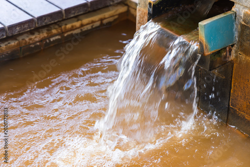 Foto Hot onsen water flowing from a wooden pipe into a bath