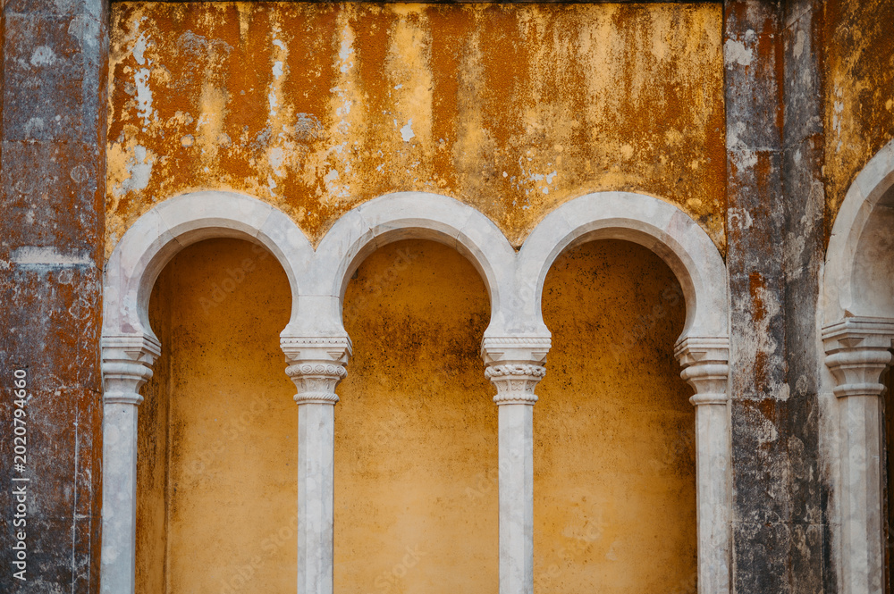 Fototapeta premium Weathered yellow wall with decorative arches at Pena Palace, Sintra