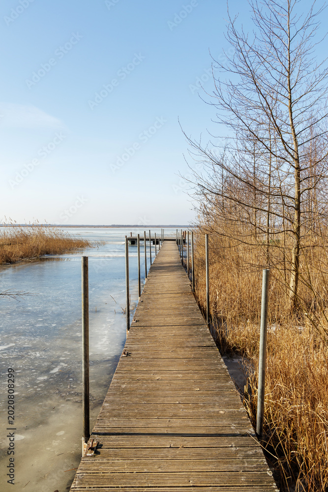 Fototapeta premium Perspective of Wooden Pier Over Frozen Lake in Spring