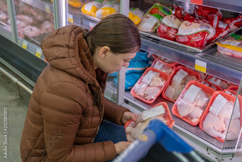 Photography Woman reading frozen chicken label closely, checking ingredients and expiry whil