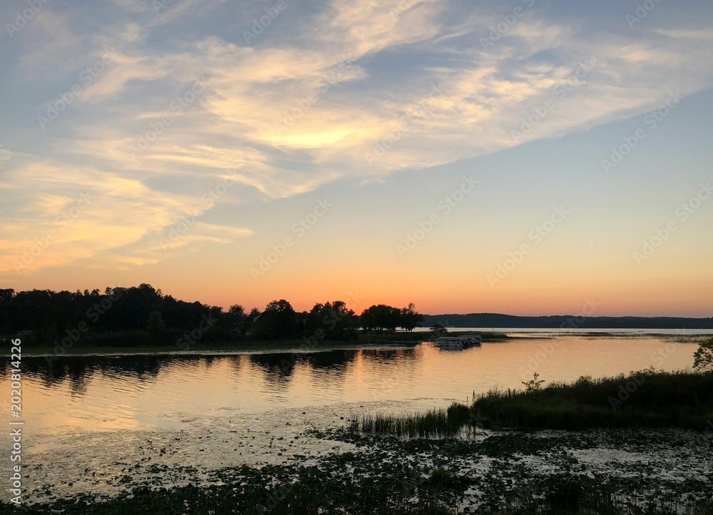 Obraz premium Stunning sunset over a calm river bordered by lush forests and rolling hills. Warm evening light reflects on the tranquil water, creating a peaceful natural landscape ideal for themes of wilderness