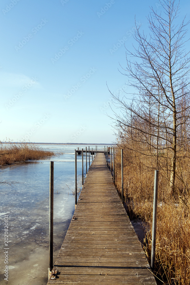 Fototapeta premium Perspective of Wooden Pier Over Frozen Lake in Spring