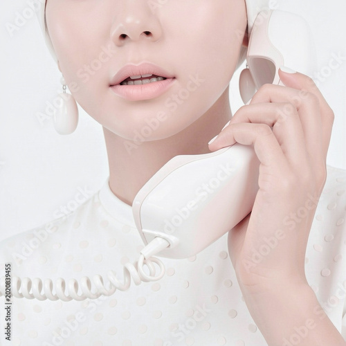 Minimalist close-up portrait of a woman holding a white retro telephone receiver against a white background