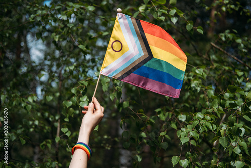 Hand holds inclusive pride flag against foliage. lgbt pride parade, queer cultural celebration, dynamic pride march, community gathering.
