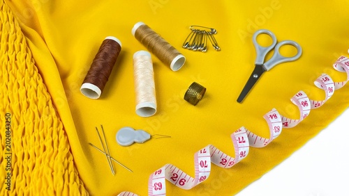 Foto On the yellow fabric there are scissors, needles, pins, a measuring tape, a thim