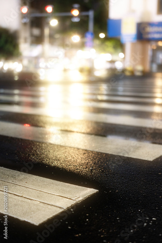 Wet City Street Crosswalk at Night with Blurred Traffic Lights and Reflections on Rain-Slicked