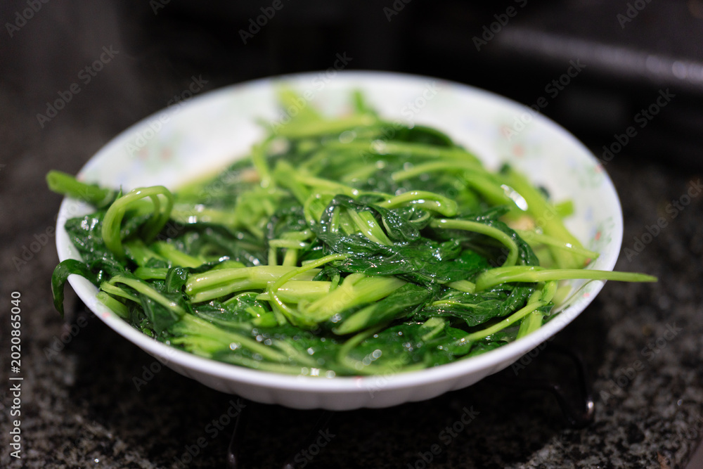 Obraz premium Steamed Spinach with Garlic in a White Ceramic Bowl on Dark Granite Surface