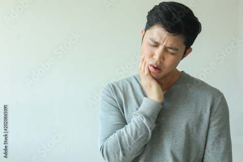 close up young asian man frown and use hand to massage on cheek after feeling pain or hurt from tmj muscle symptom at home for un healthy lifestyle and treatment concept
