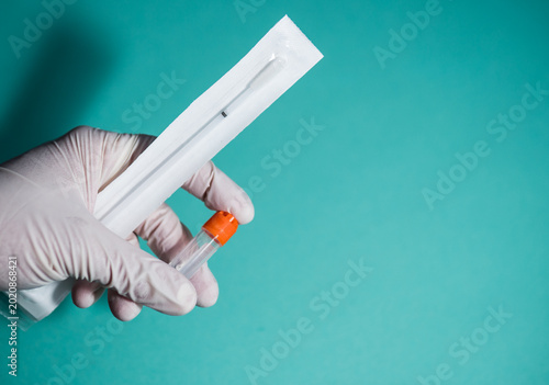 Tableau sur toile Close-up of gloved hand holding laboratory sample tube and sterile swab kit against blue background