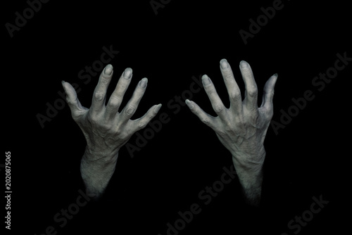Bony pale and sinewy male hands with long nails reach up out of the total darkness. Dark and creepy supernatural atmosphere.
