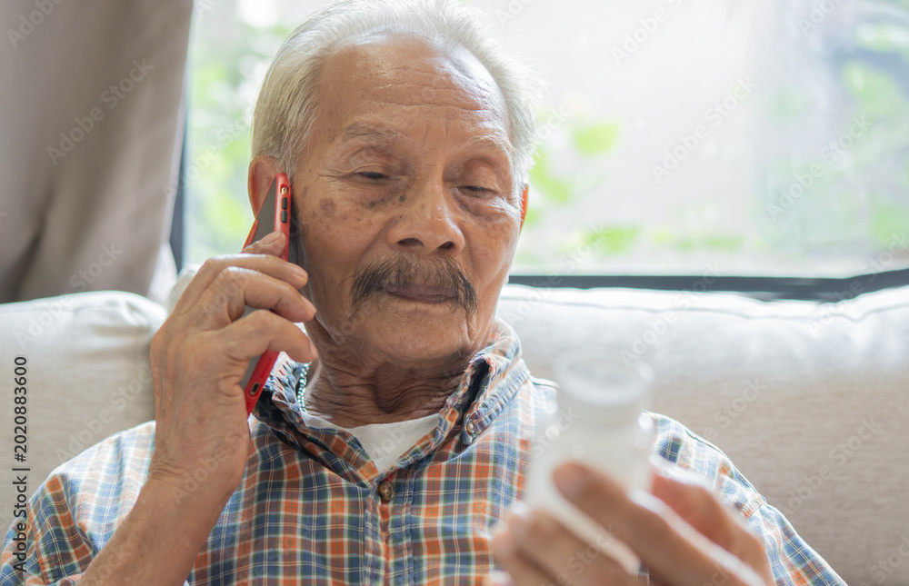Φωτογραφία Healthy senior Asian man reading prescription bottle and talking on his cell pho