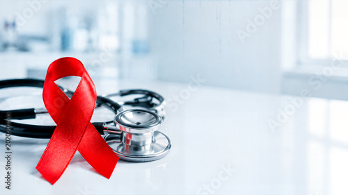 Red ribbon for HIV and AIDS awareness with a medical stethoscope. World AIDS Day and healthcare concept on a blurred hospital background with copy space