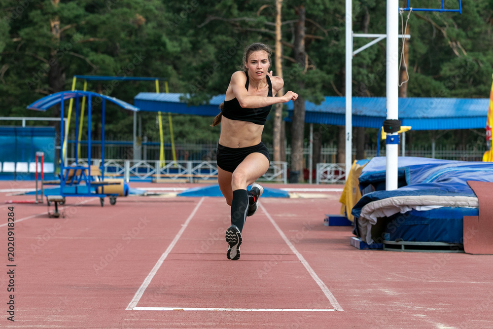 Fototapeta premium Beautiful female athlete triple jump in training at stadium