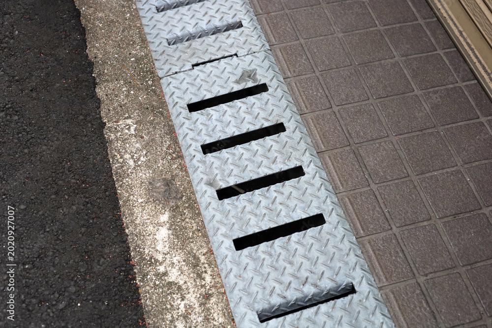 Fototapeta premium Steel drainage grate on sidewalk near shop entrance
