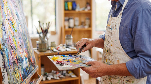 Tableau sur toile Mature male artist intently working on a vibrant abstract oil painting in his brightly lit art studio