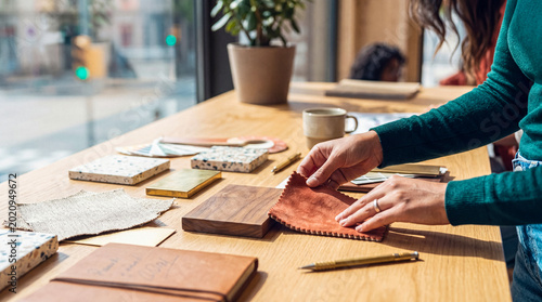 Fényképezés Hands selecting a brown suede fabric swatch from various material samples on a large wooden table in a design studio