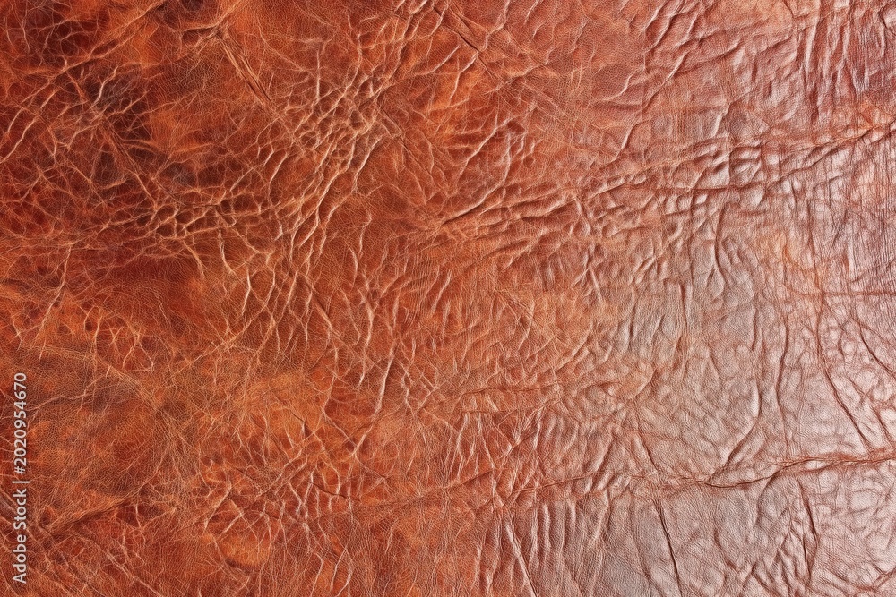 Fototapeta premium Close-up of textured brown leather showing natural creases and fine cracks, highlighting its rich color and detailed surface pattern.