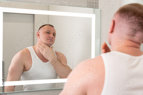 Fotografie Handsome young man looking at his reflection in bathroom mirror after shaving