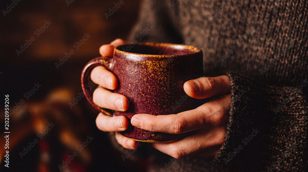 Αυτοκόλλητο A person's hands gently holding a rustic, textured ceramic mug, evoking feelings of warmth, comfort