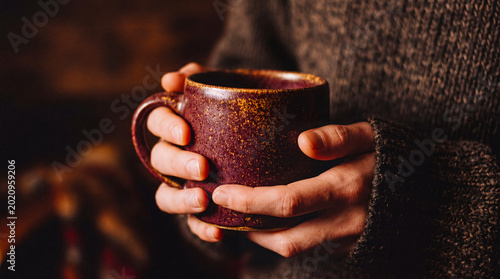 Photos A person's hands gently holding a rustic, textured ceramic mug, evoking feelings of warmth, comfort