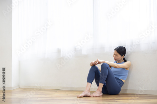 Quadro em tela Asian Woman in Yoga Wear Sitting on Floor with Exhausted Expression