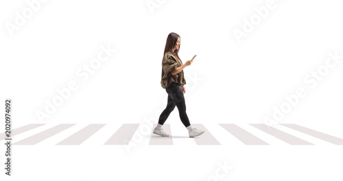 Young woman crossing a street and looking at her smartphone