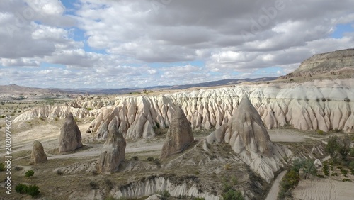 Detailed view of white volcanic tuff ridges and cone-shaped rock formations in Cappadocia valley under a cloudy sky.