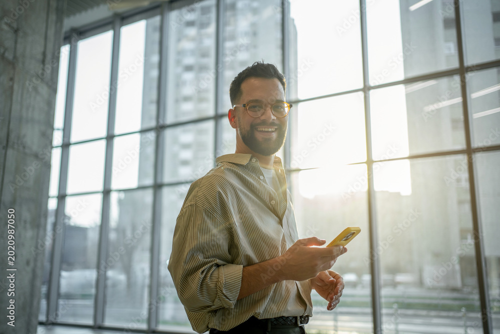 Foto Young man smiling while using smartphone in modern workspace