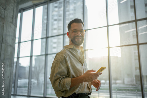 Young man smiling while using smartphone in modern workspace