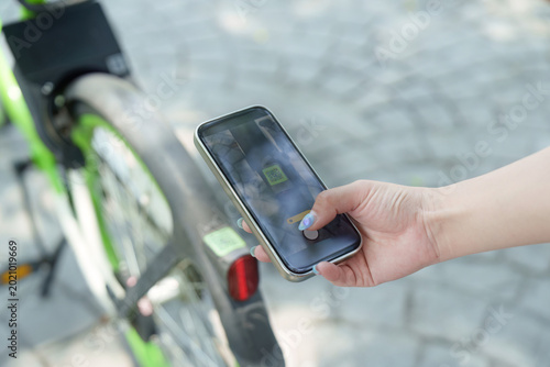 Asian woman scanning QR code on smartphone to rent shared bicycle outdoors, technology
