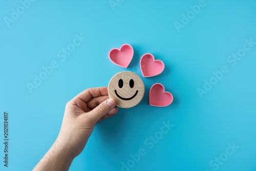 A hand holds a smiley face with three hearts on a blue background