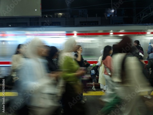 Schilderij op canvas A dynamic long-exposure shot of a crowded train station platform at night, featuring the motion blur of commuters and a passing train
